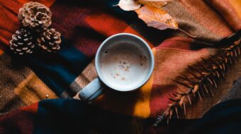 warm drink in a mug on a plaid tablecloth with leaves and pinecones around it