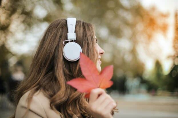 woman holding a leaf while listening to a relaxing playlist with headphones in the park